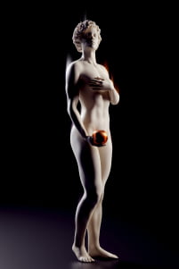 A statue portraying a naked woman covering parts of her body and holding a ball in her hand.